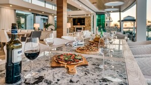 A dining area with a marble table, wine glasses, and bottles, featuring pizzas and a view of the outdoors. - Luxury Ghost Estate on the Noosa Sound (Noosaville)
