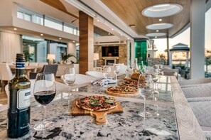 Un espace repas avec une table en marbre, des verres à vin et des bouteilles, où l’on sert des pizzas, et qui offre une vue sur l’extérieur.