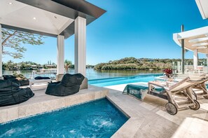 Un espace piscine extérieur moderne, doté de chaises longues, d’une petite table de billard et offrant une vue sur un lac et des collines.