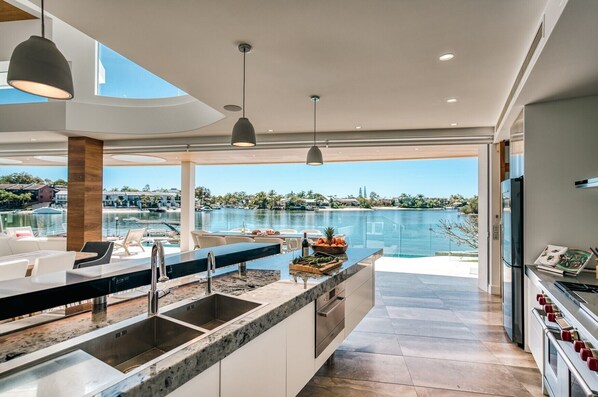 Une cuisine moderne dotée d’un grand îlot central, un coin repas offrant une vue sur la piscine et un vaste espace de vie avec vue sur l’eau.