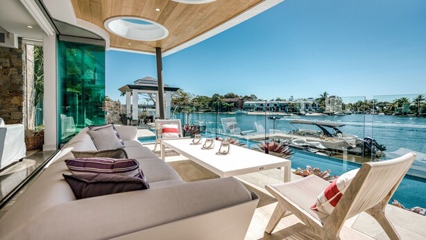 A modern outdoor lounge area with a pool view, featuring a sofa, chairs, and a dining table. - Luxury Ghost Estate on the Noosa Sound (Noosaville)