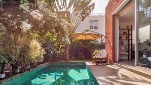 Une piscine dotée d’une terrasse carrelée, entourée d’une végétation luxuriante et agrémentée d’un espace patio avec des meubles d’extérieur.
