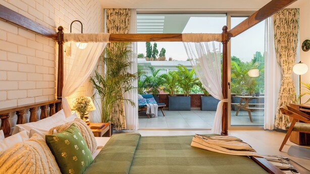 Une chambre à coucher avec un lit, des rideaux et une vue sur un espace extérieur aménagé pour s’asseoir.