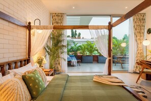 Ein Schlafzimmer mit Bett, Vorhängen und Blick auf einen Außenbereich mit Sitzgelegenheiten.