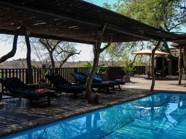 Zona de piscina con sillones de descanso y un espacio de estar cubierto.
