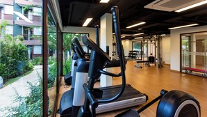 A gym with exercise equipment, a view of a residential building, and a wooden floor.