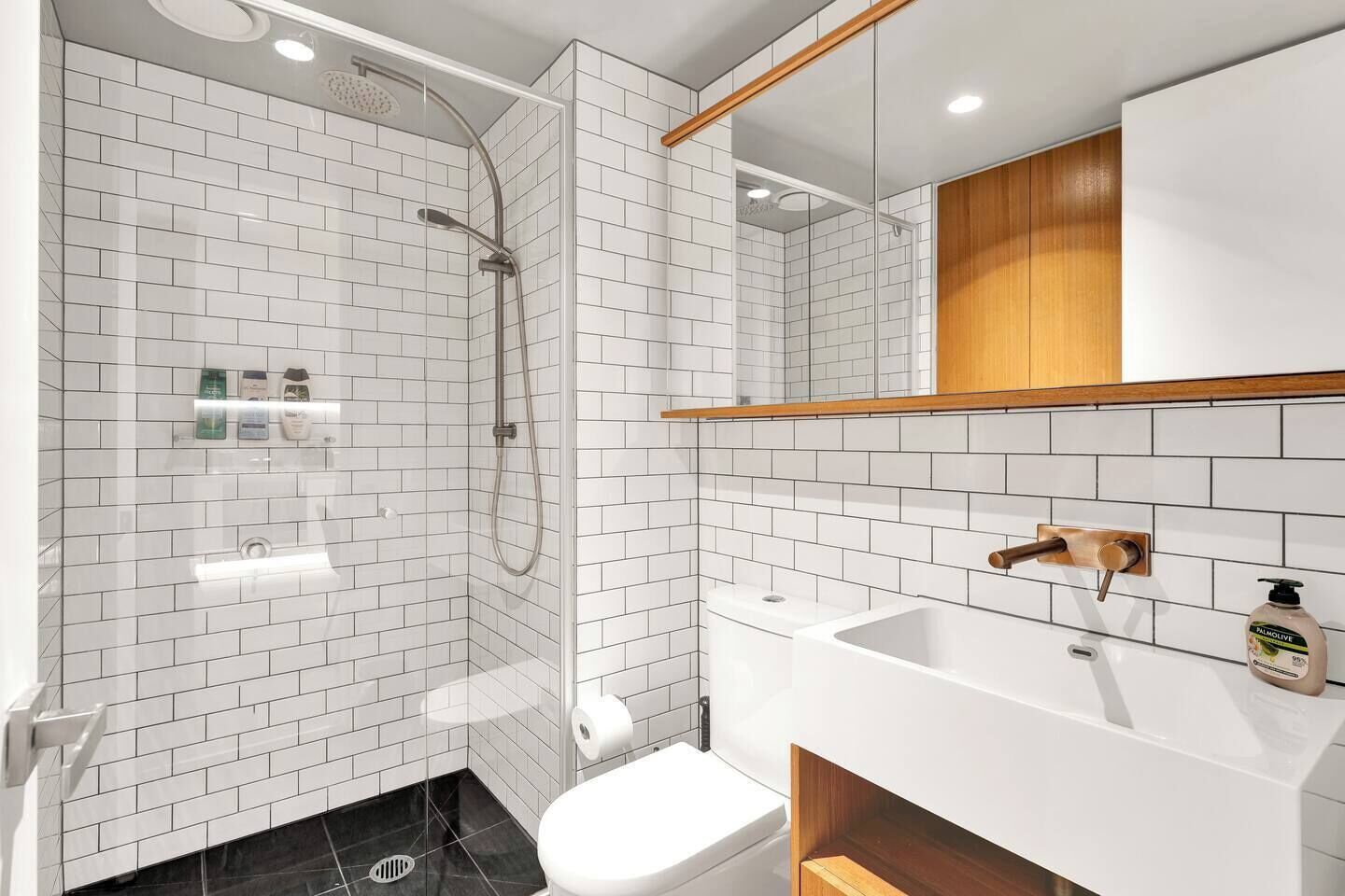 Ein modernes Badezimmer mit weißen Feldbahnschiefern, einer gläsernen Dusche, einem weißen Waschbecken und einem hölzernen Waschtisch.