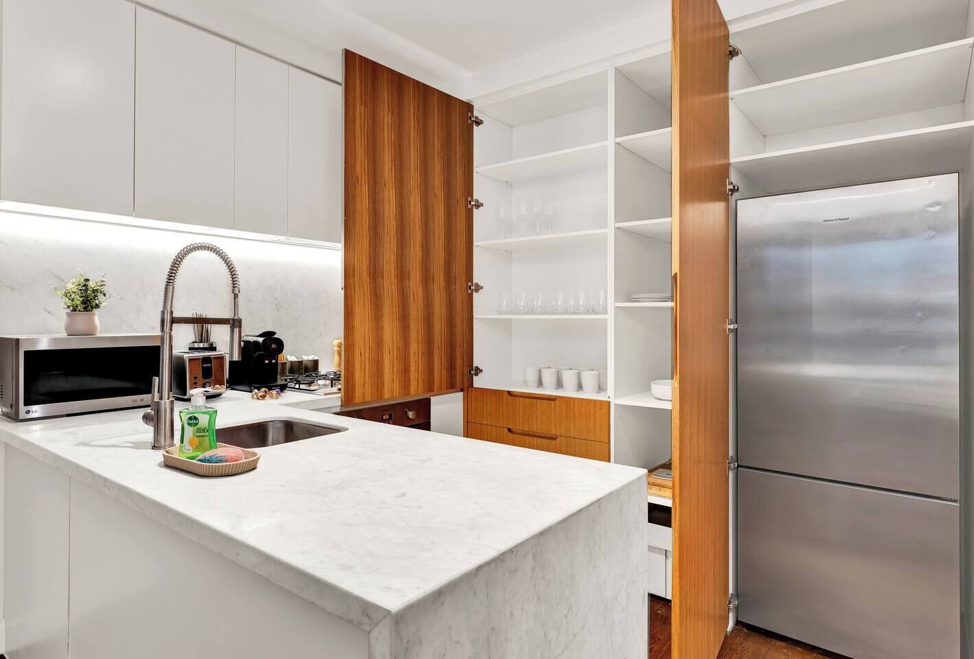 A modern kitchen with white cabinetry, a stainless steel refrigerator, and a wooden cabinet door.