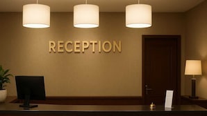 A reception desk with a sign that reads "RECEPTION" above it. There are three pendant lights above the desk, a potted plant to the left, and a desk lamp to the right.