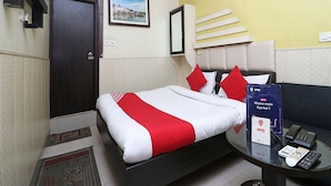 A hotel room with a bed, a bedside table with a phone and a remote control, a wall clock, and a framed picture on the wall.