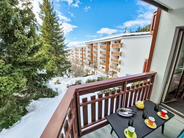 Ein Balkon mit Frühstückstisch, mit Blick auf ein schneebedecktes Gebäude mit Balkonen.