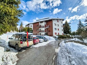 Ein Hotel mit modernem Design, das durch seine mehrstöckige Bauweise mit Balkonen gekennzeichnet ist. Vor dem Gebäude sind mehrere Autos geparkt, und Schnee liegt auf dem Boden und um das Gebäude herum.