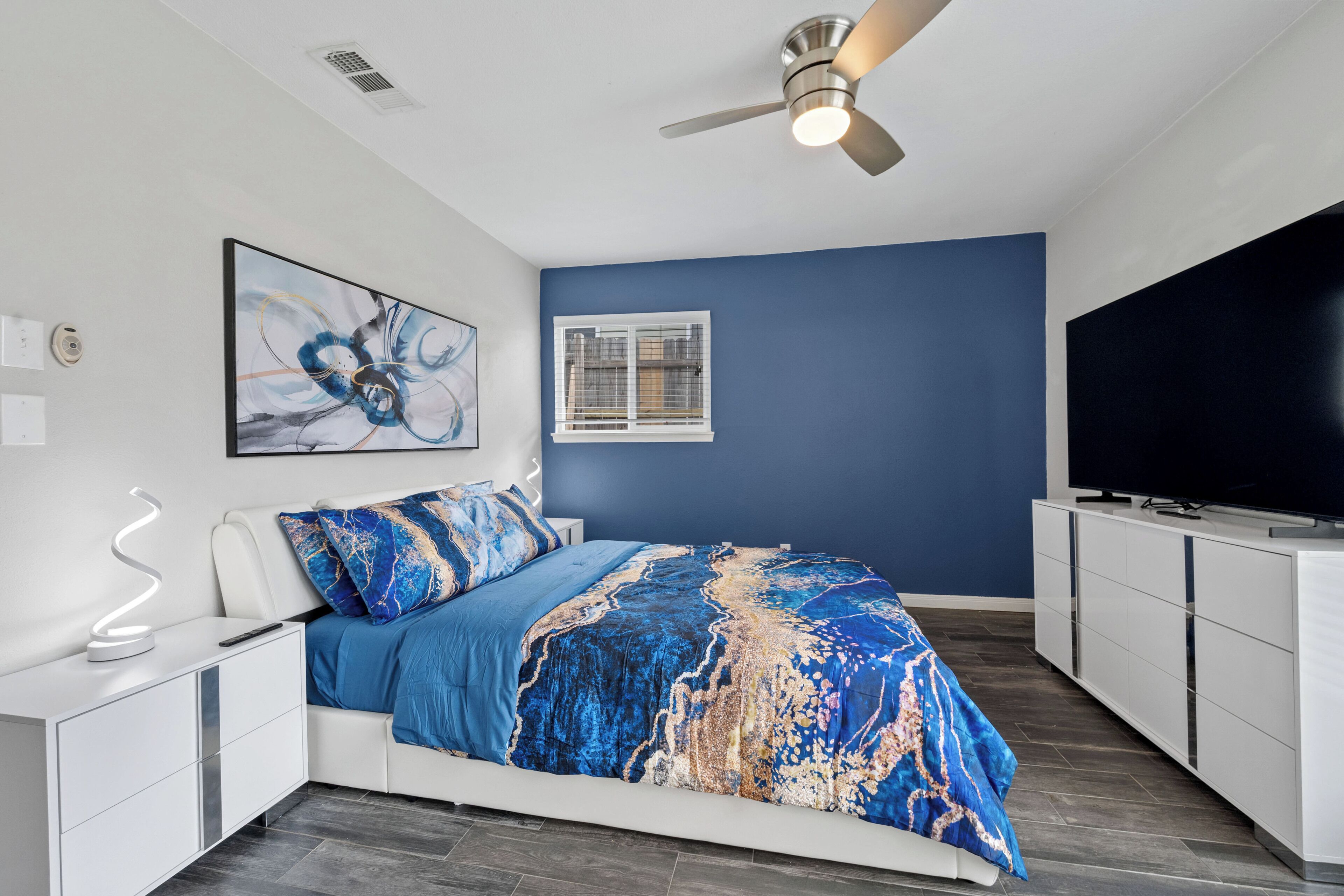 Une chambre moderne avec un lit, un ventilateur de plafond, une télévision et une fenêtre.