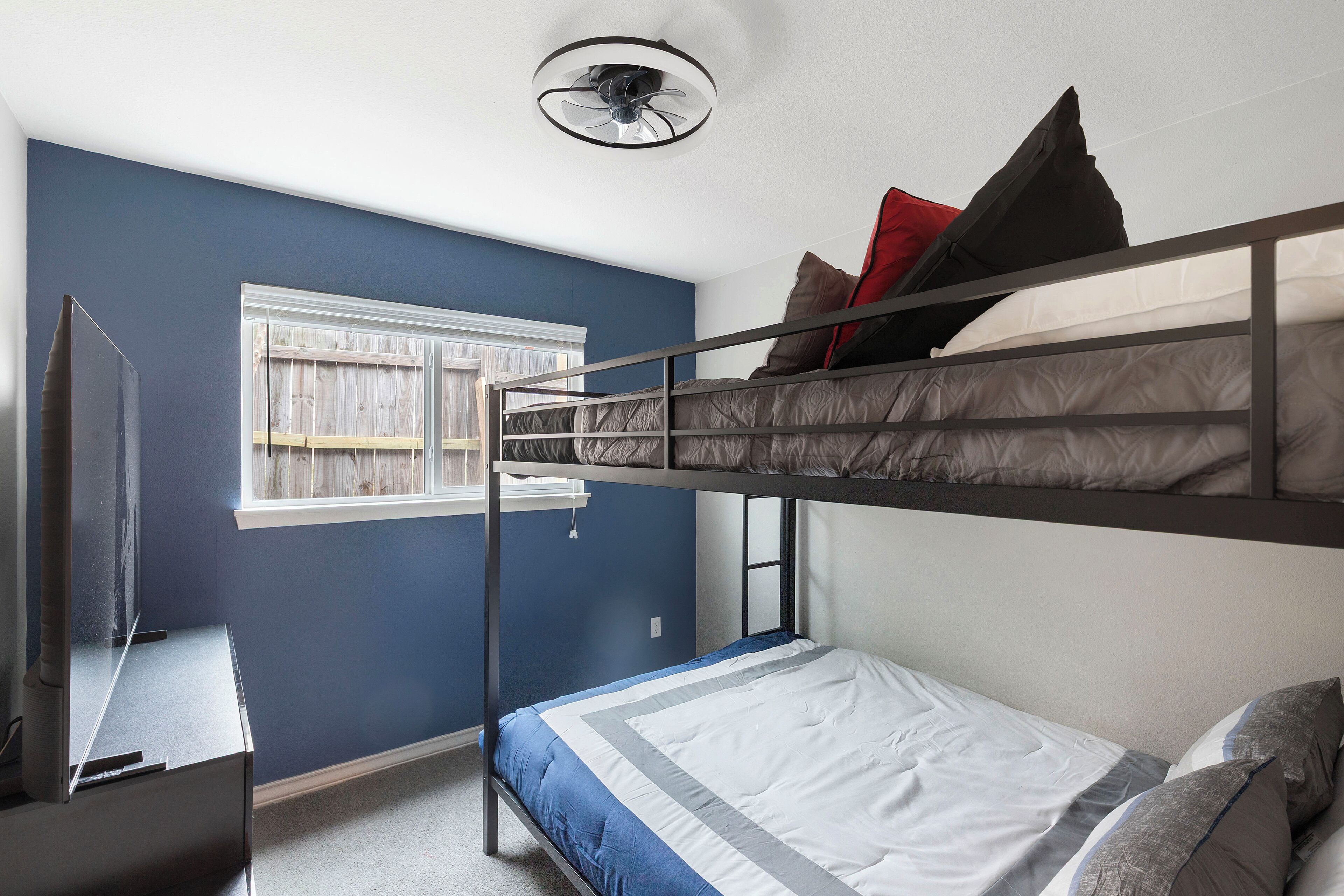 A bunk bed room with a window, a ceiling fan, and a television.