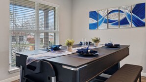 Uma sala de jantar com uma mesa comprida posta para quatro pessoas, um banco e uma janela com persianas.