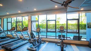 Academia com esteiras, elíptica e remo, com vista para uma piscina.