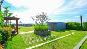 Um jardim bem cuidado com um pérgola, um pequeno galpão e um céu limpo.