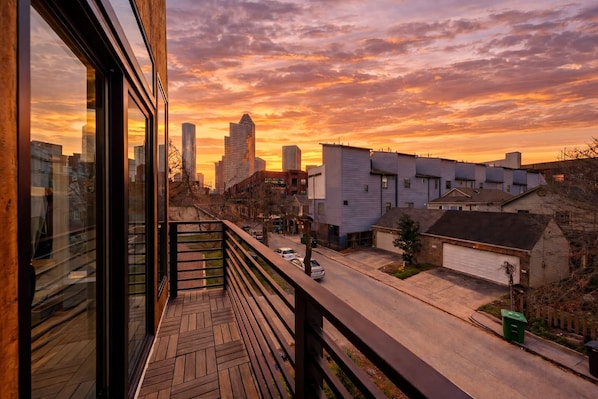 Un balcón con vistas a un paisaje urbano al atardecer, con edificios modernos y cielo despejado.