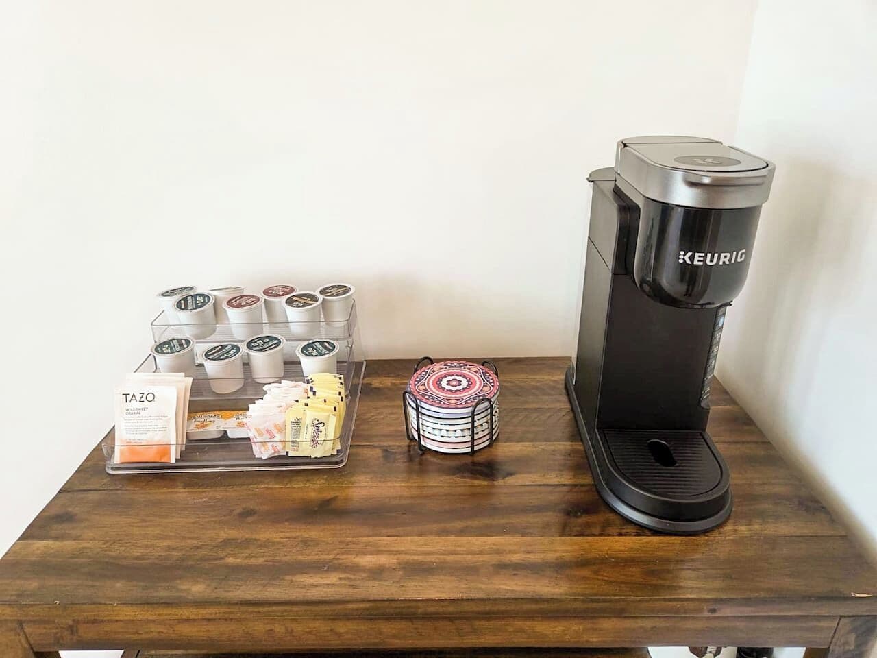 Une machine à café et un plateau avec des dosettes de café et des sachets de thé, posés sur une table en bois.