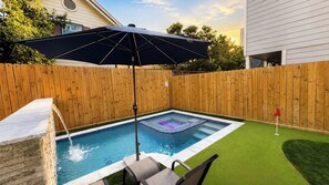 Patio trasero con piscina, cerca de madera, área de patio con una silla y una bandera roja.