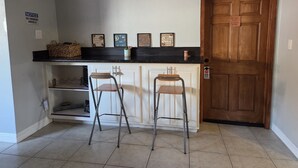 Une cuisine avec un plan de travail noir, deux tabourets de bar, une porte en bois et un panneau indiquant « Accès interdit aux visiteurs ».