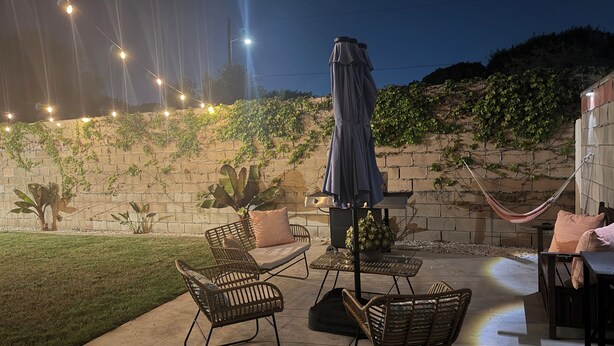 Un espace extérieur aménagé en terrasse, avec des chaises en métal, une table, un hamac et des guirlandes lumineuses.