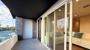 Een modern balkon met een glazen deur die leidt naar een woonruimte met een bank en kussens.