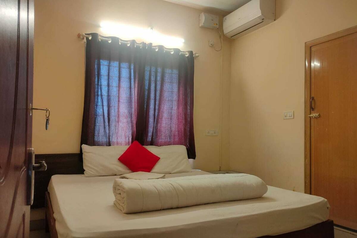 A hotel room with a bed, curtains, an air conditioning unit, and a door.