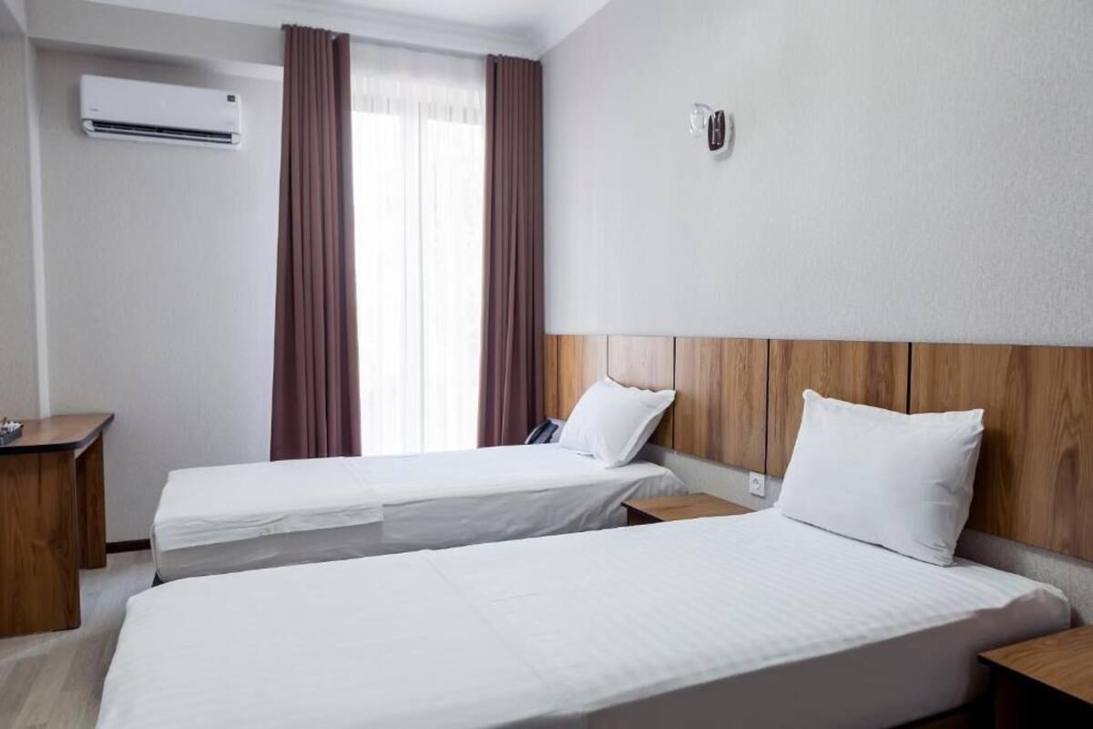 Habitación de hotel con dos camas individuales, un cabecero de madera, un escritorio y un equipo de aire acondicionado.