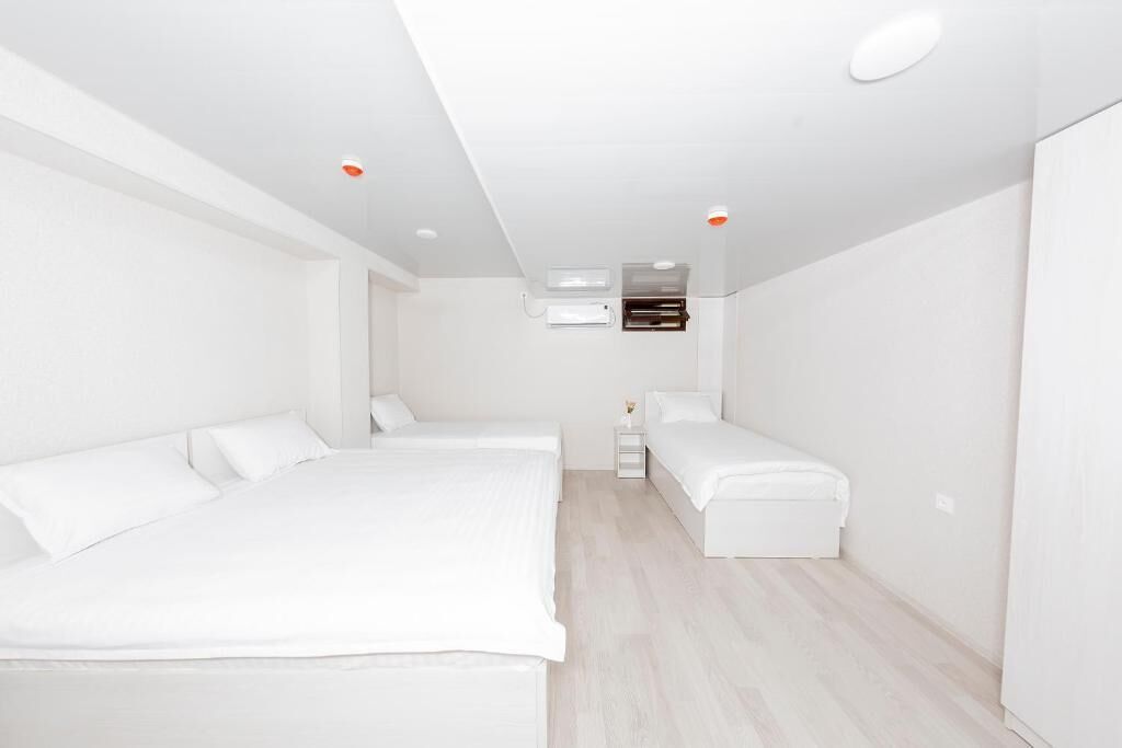 A modern, white-themed bedroom with two beds, a small bedside table, and a built-in air conditioning unit.