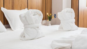 Une chambre d’hôtel avec une tête de lit en bois, des serviettes blanches soigneusement pliées sur le lit et un vase avec des fleurs en arrière-plan.