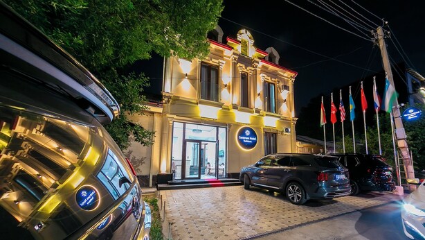 Un hôtel à la façade classique, doté d’une entrée bien éclairée et orné de plusieurs drapeaux à l’avant.