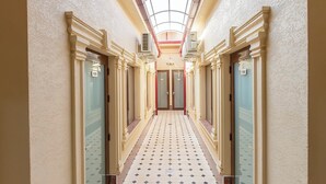 Un couloir d’hôtel avec une verrière, un sol carrelé et des portes portant des numéros.