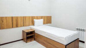 Une petite chambre à coucher, bien rangée, avec une tête de lit en bois, un lit simple, une table de chevet et un radiateur.