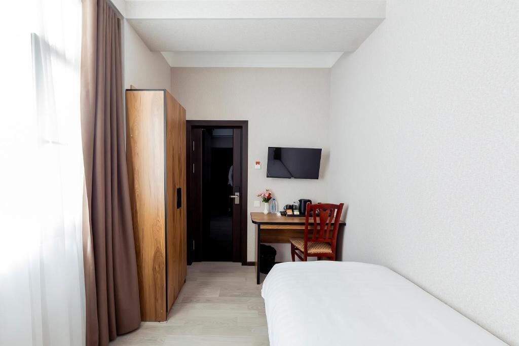 Ein Hotelzimmer mit Bett, Schreibtisch mit Stuhl, Fernseher an der Wand und Kleiderschrank.