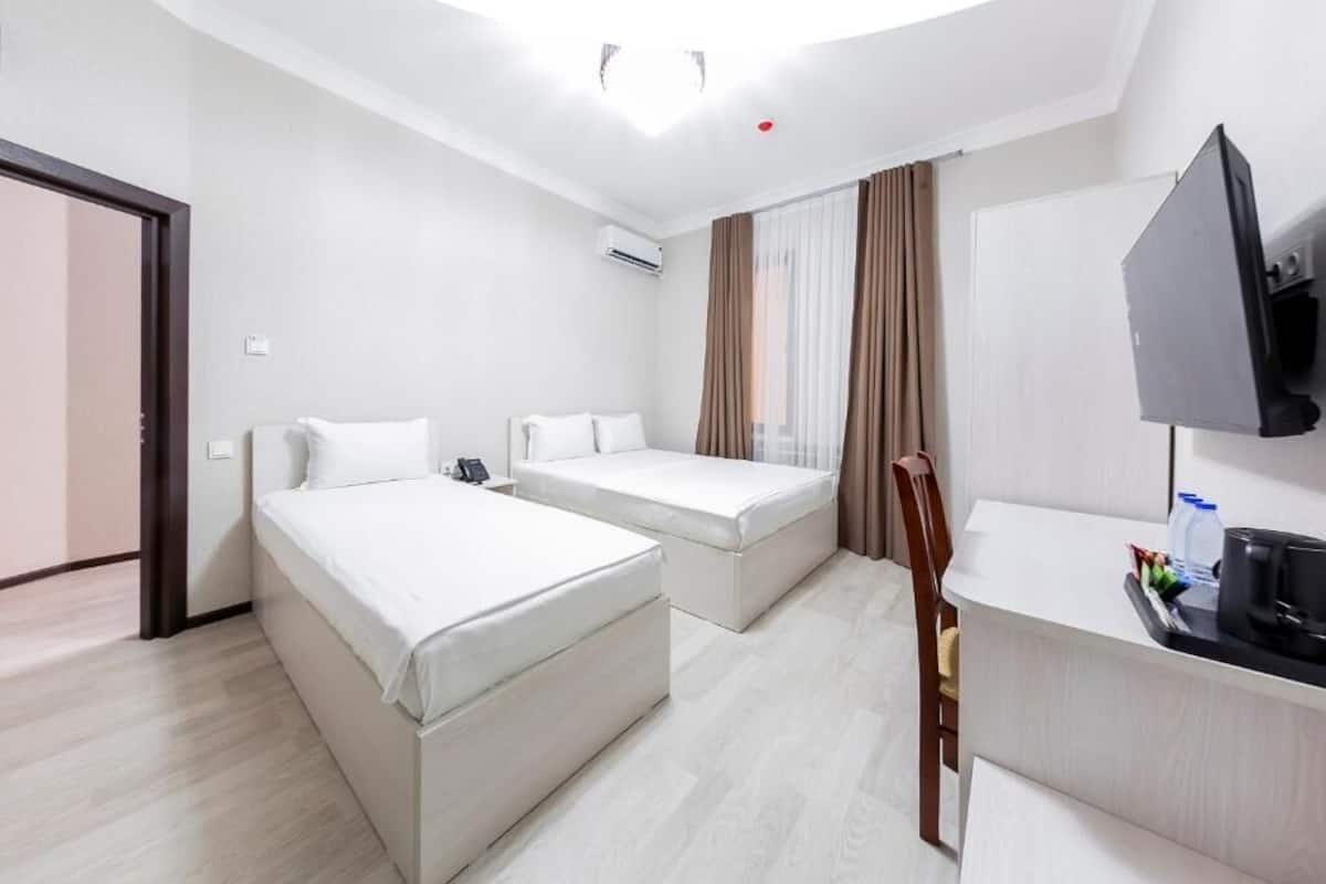 Una habitación de hotel con cama, escritorio con televisor y ventana con cortinas.