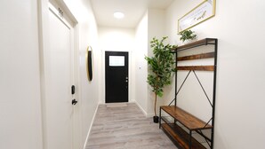 En hall med en svart dörr, en träbänk, en krukväxt och en inramad skylt på väggen.