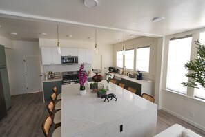 A modern kitchen with white cabinets, a marble island, pendant lighting, and a dining area with chairs. - Spacious & Luxury Seattle Oasis: Sauna, Hot Tub & Capitol Hill Proximity (Seattle)