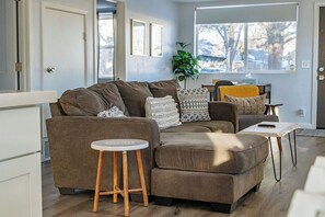 Ein Wohnzimmer mit einem braunen Sofa, einem kleinen runden Tisch und einem Fenster mit Blick auf Bäume.