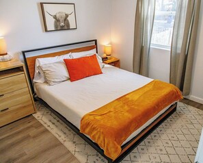 Un lit bien fait, avec une literie blanche et orange, une tête de lit en bois et une table de chevet avec une lampe.