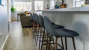 Ett modernt kök med en bardisk, trästolar och utsikt över vardagsrummet.
