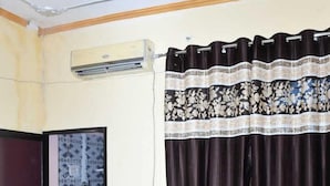A room with a bed, a chair, a small table, an air conditioner, a curtain, and a door with a patterned wall. - Sarla Resort (Sawai Madhopur)