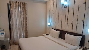 A hotel room with a bed, a bedside table, a nightstand, a lamp, a curtain, and a wall with a bamboo pattern. - Sarla Resort (Sawai Madhopur)