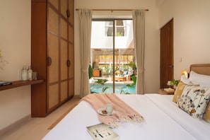 A hotel room with a bed, a bedside table, a view of a pool, and a sliding door leading to an outdoor area. - TBK VILLA  VAGATOR R4 (Vagator)
