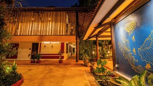 A building with a bamboo exterior, a covered outdoor area with potted plants, and a large map mural. - Kampung Kamboja (Siem Reap)