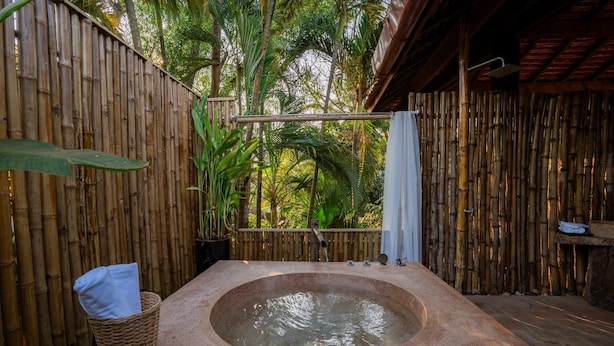 A hot tub in a bamboo-walled outdoor area with a hanging shower and a basket with a towel. - Kampung Kamboja (Siem Reap)