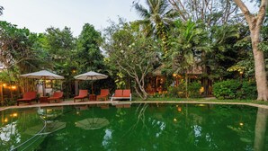 A serene pool area with lounge chairs and umbrellas, surrounded by lush greenery and trees. - Kampung Kamboja (Siem Reap)