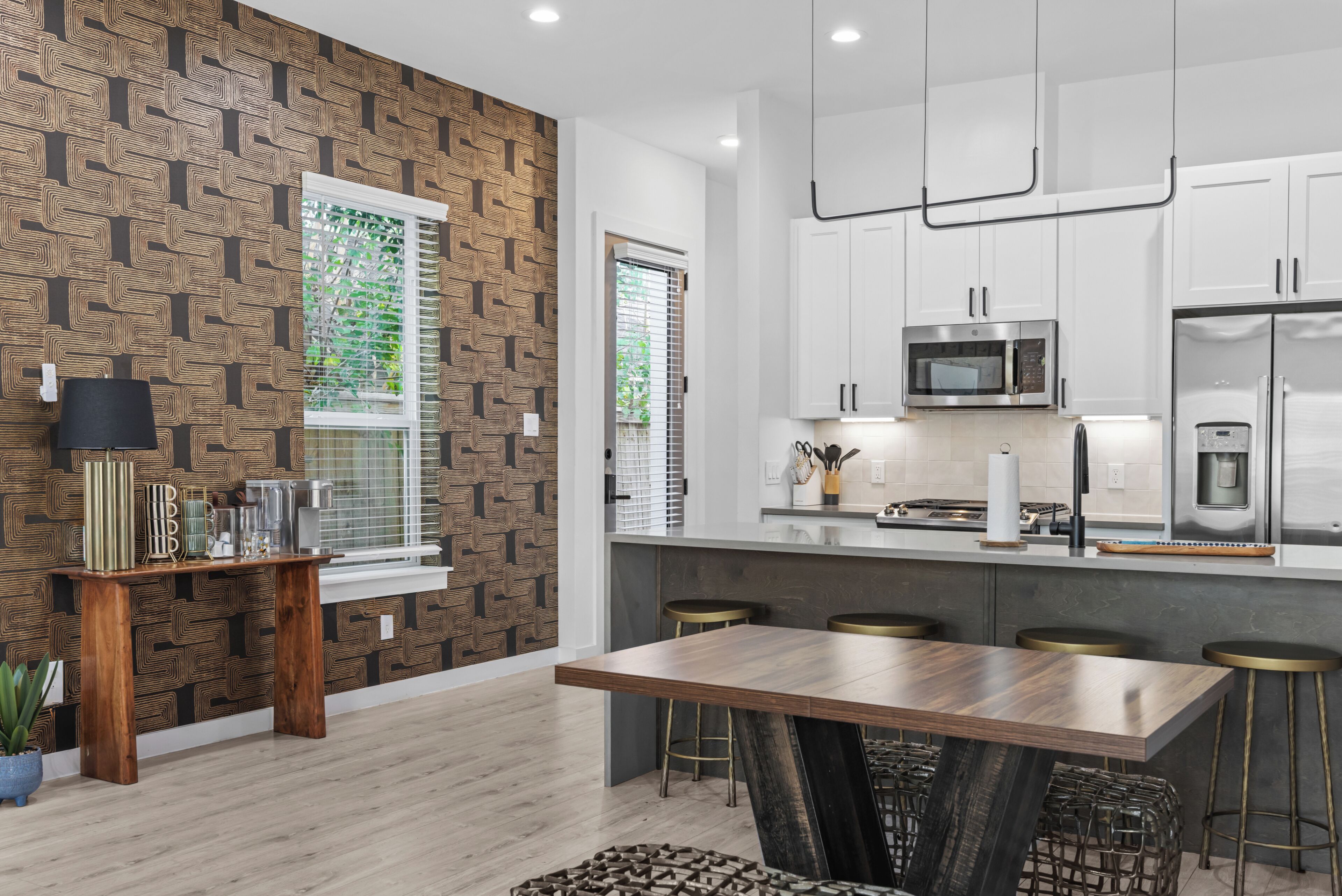 A modern kitchen with white cabinets, a wooden dining table, and a patterned wall.