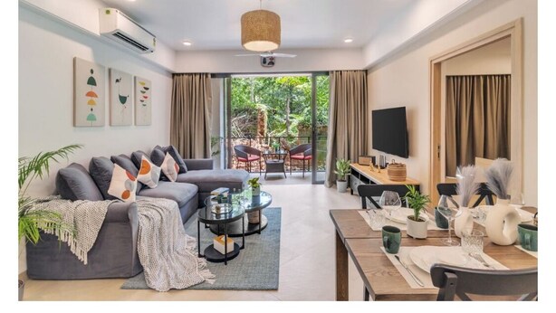 Ein modernes Wohnzimmer mit Sofa, Couchtisch und Essbereich. Ein Fernseher ist an der Wand befestigt, und es gibt einen Balkon mit Gartenmöbeln.