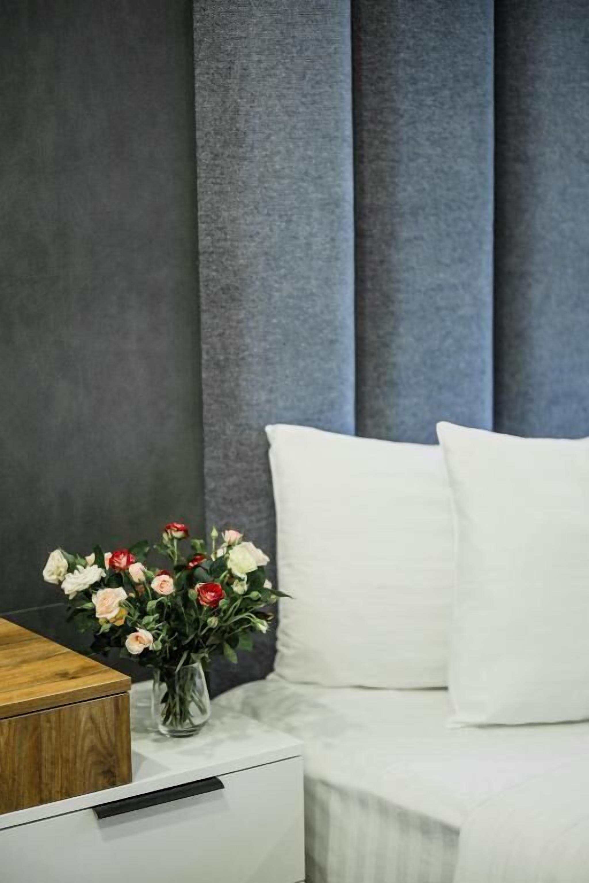A bedroom with a bed, white pillows, a nightstand, and a vase of flowers.